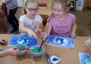 Dzieci przy stoliku malują niebieską farbą wodę na naszej planecie